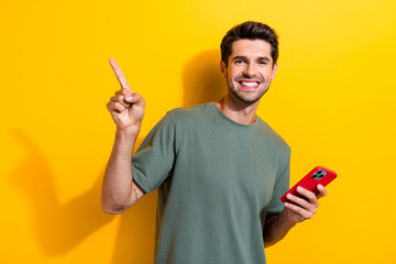 Photo of positive clever man dressed khaki t-shirt hold smartphone indicating at offer empty space...