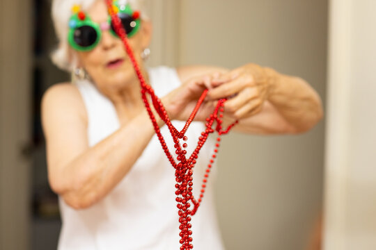 elderly lady in fun Christmas glasses trying to untangle string of red beads