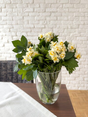 white and yellow daffodil flowers in vase on table in living room over brick wall