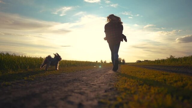 teen girl running with a dog in the park. happy family freedom a kid dream concept. silhouette of a teenage girl running along the road in the park at sunset view from the back with a shaggy sun dog