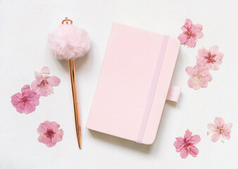 Pink notebook, decorative fur pen and dried sakura flowers on white top view, textbook mockup