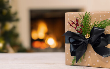 Decorated Christmas gift box with black bow on background of burning fireplace and christmas tree