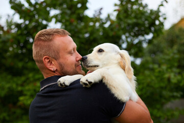 Man Smiling While Holding A Playful Golden Retriever Puppy Outdoors In Summer