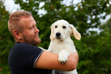 Man Smiling While Holding A Playful Golden Retriever Puppy Outdoors In Summer