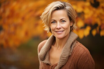 Portrait of a happy woman in her 50s dressed in a warm wool sweater against a background of autumn...