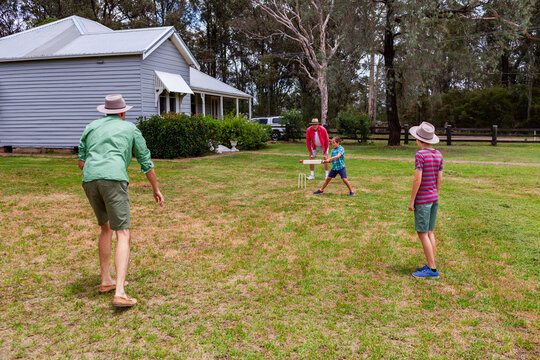 Young aussie boys playing backyard cricket with dad and grandfather in front yard of house