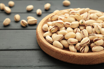 Salted pistachios for beer on black background. Healthy delicious pistachios in wooden plate.