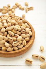 Salted pistachios for beer on white background. Healthy delicious pistachios in wooden plate. Vertical photo