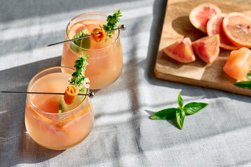 Summer refreshing grapefruit drink or alcoholic cocktail with grapefruit slices, ice and herbs. Citrus detox drink.