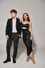 full length of elegant couple in evening attire standing together on grey background, night out