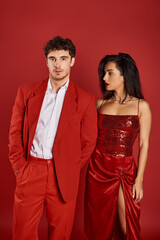 elegant young woman with red lips seducing handsome man posing on red background, hand in pocket