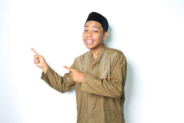smiling asian muslim man wearing koko clothes pointing to beside with excitement expression looking...