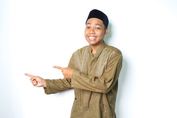 smiling asian muslim man wearing koko clothes pointing to beside with excitement expression looking...