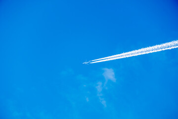 Distant passenger jet plane flying on high altitude on clear blue sky leaving white smoke trace of contrail behind. Air transportation concept.