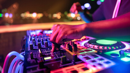 Fototapeta na wymiar Detalhe da mão de um dj manuseando os botões de um controlador, em uma festa com muitas luzes coloridas.