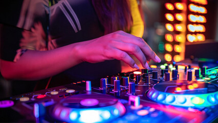 Close em mão feminina, manuseando os botões do controlador de dj, durante uma festa com muitas luzes coloridas.