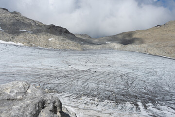 Hikers traverse a vast glacier under a cloud-covered sky