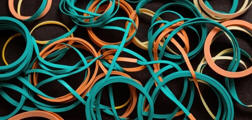  a pile of multicolored rubber bands sitting on top of a black cloth covered in brown, blue, orange, and yellow rubber bands with a black background.
