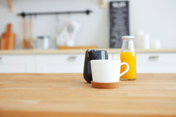 Wooden table with mug, milk jug and orange juice with blurred kitchen background