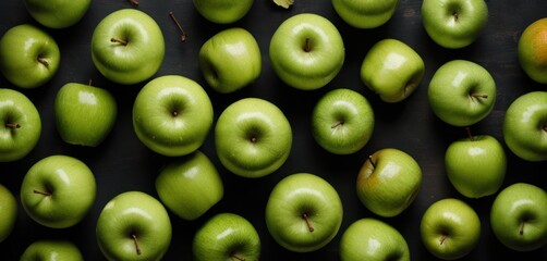  a group of green apples sitting next to each other on top of a black surface with a leaf sticking out of the middle of the top of one of the apples.