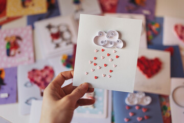 Hand holding quilling card with cloud and hearts rain. Love concept. Happy valentine day, dating,romantic or wedding. Gift, message for lover. Hand made of paper quilling technique. Hobby, home office