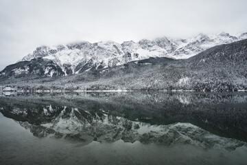 Fototapeta na wymiar Snowy mountains reflecting in a tranquil lake with overcast skies