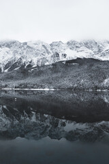 A serene winter landscape with a snow-covered mountain reflecting on a calm lake.