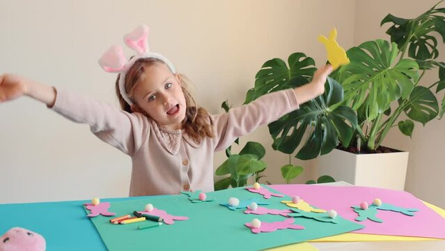 Happy child girl in bunny ears make and play Easter paper colored garland Easter bunny. Children crafts for Easter party at home. Holiday Art Activity Kid. Fine motor skills, creativity and hobby DIY