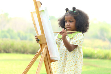 Cute smiling African girl with black curly hair painting on canvas at green garden outdoor. Kid drawing nature picture in green summer park. Happy little child having fun while spending time outdoors. - obrazy, fototapety, plakaty