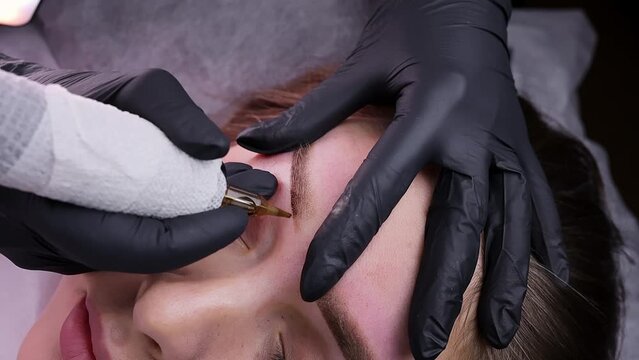 Performing beautiful permanent eyebrow makeup and applying pigments to the skin of the eyebrows. Permanent makeup procedure, performing PMU of eyebrows