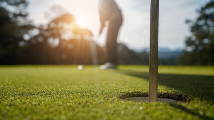 Golfer putting ball on the green golf, lens flare on sun set evening time.