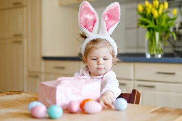 Cute little toddler girl wearing Easter bunny ears playing with colored pastel eggs. Happy baby...