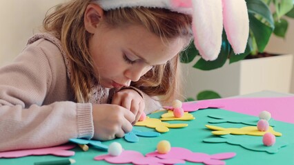 Child girl in rabbit ears creating Easter paper colored garland Easter bunny. Cute children's...