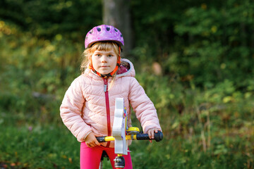 Child riding balance bike. Kids on bicycle in sunny forest. Little girl enjoying to ride glider...