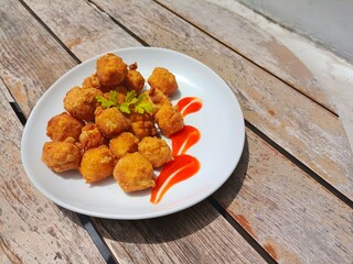 Crispy tofu with a little sauce next to it on a white plate, and placed on a wooden table