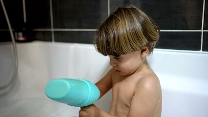 Little boy inside bathtub playing with plastic toy object, one male caucasian kid seen through glass during night-time bath-time routine
