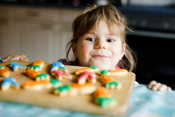 Cute little toddler girl and fresh baked homemade Easter or spring cookies at home indoors....
