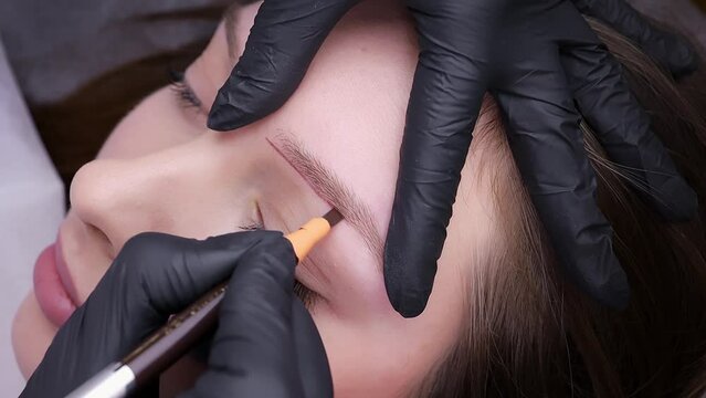 Applying a pencil sketch to the eyebrow contour before the treatment. Permanent makeup procedure, performing PMU of eyebrows