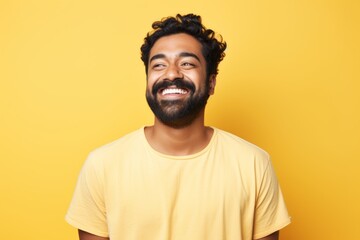 Fototapeta premium Portrait of a grinning indian man in his 30s donning a trendy cropped top against a pastel yellow background. AI Generation