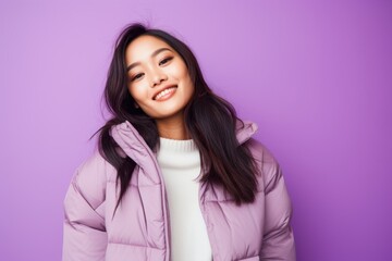 Fototapeta premium Portrait of a joyful asian woman in her 20s sporting a quilted insulated jacket against a pastel purple background. AI Generation