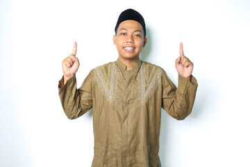 asian muslim man pointing to above and smiling at camera wearing islamic dress isolated on white...