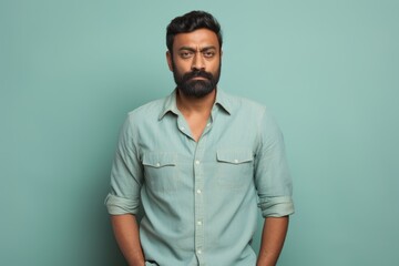Obraz premium Portrait of a content indian man in his 30s sporting a versatile denim shirt against a pastel teal background. AI Generation