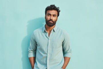 Portrait of a content indian man in his 30s sporting a versatile denim shirt against a pastel teal background. AI Generation