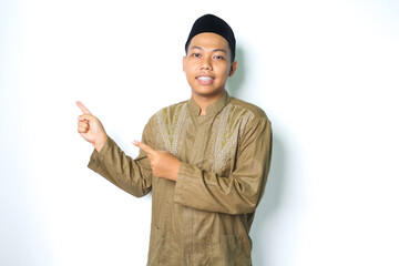 smiling asian muslim man pointing to the right side wearing islamic dress isolated on white...