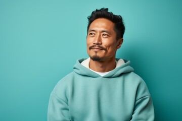 Fototapeta premium Portrait of a tender asian man in his 40s wearing a thermal fleece pullover against a pastel teal background. AI Generation