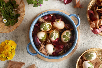 Easter eggs with green leaves attached to them are being dyed with onion peels in a blue pot, top view