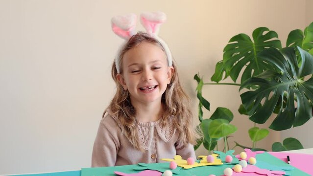 Happy toddler smile with teeth excited funny surprised child girl prepare for Easter party make paper garland colored Easter bunny DIY. Happy kids holidays. Children in bunny ears costume