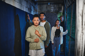 young and multicultural friends walking through secret passage in quest room, adventure and mystery