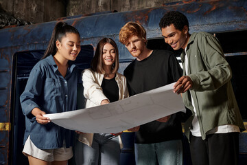 group of happy young multicultural friends solving quest task while looking at map in escape room