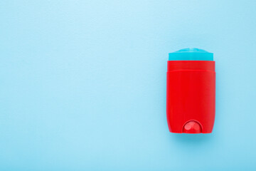 Red plastic stick of armpit deodorant on light blue table background. Pastel color. Male daily...